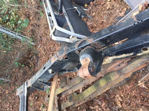 1994 Ford Bronco - Close-up of heavily rusted vehicle frame and suspension parts, lying on the ground amidst debris.