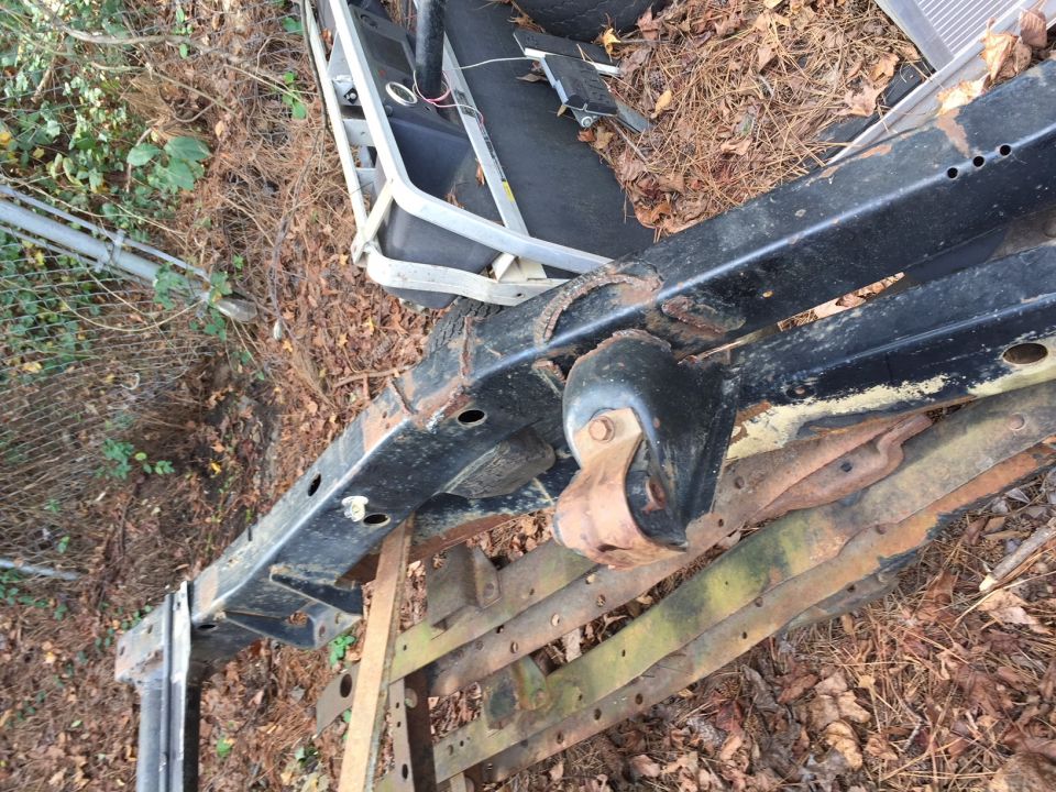 Rusted black metal frame with suspension components, resting on wooden planks outdoors