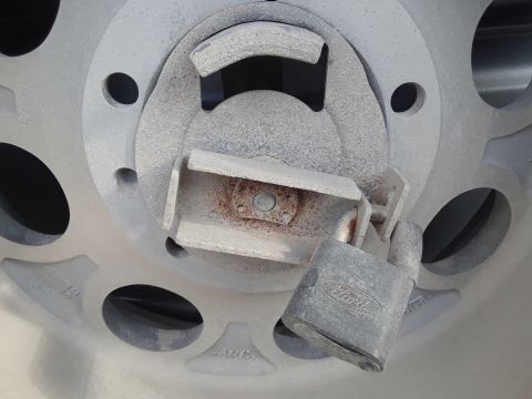 1985 Ford Bronco - Close-up of a spare tire carrier secured with a padlock bearing the Ford logo.