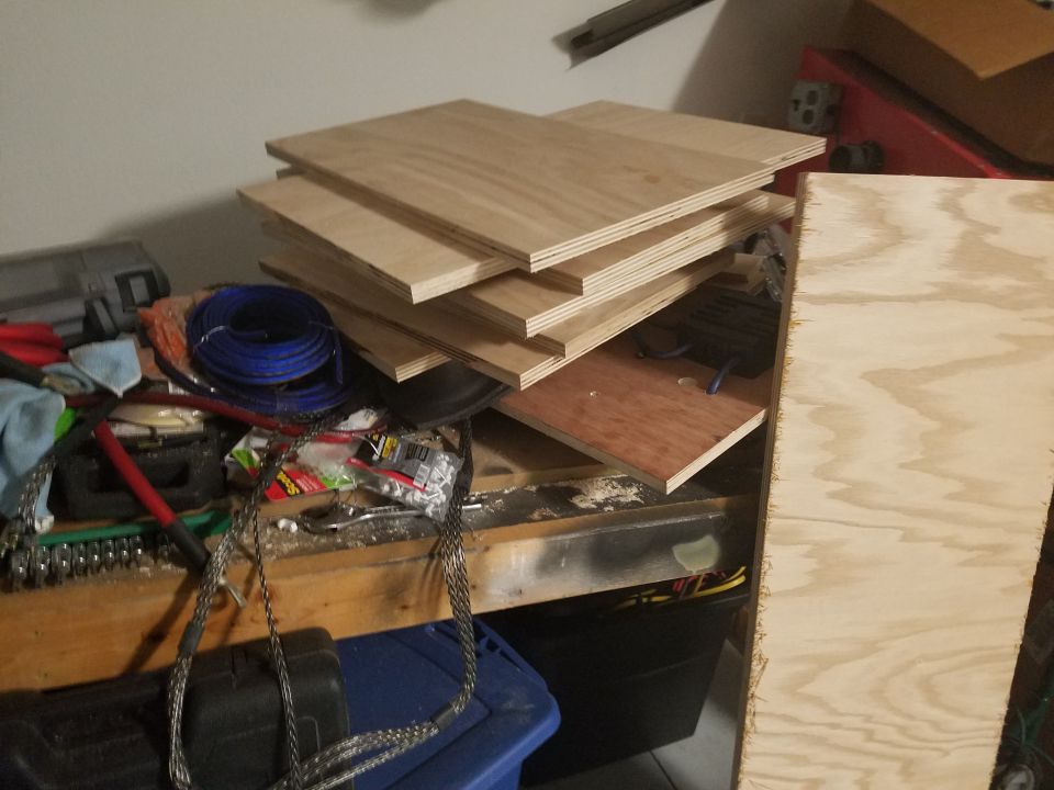 Stack of plywood sheets on a workbench with tools and wiring
