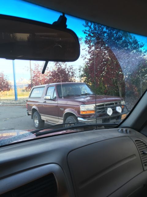 1987 Ford Bronco - This maroon SUV, likely a 1992 Ford Bronco, is seen from inside another vehicle, auxiliary lights on its front bumper.