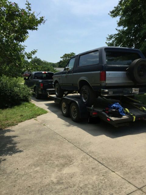 1987 Ford Bronco - A 1987 Ford Bronco is loaded onto a trailer, with a black pickup truck visible in the background.