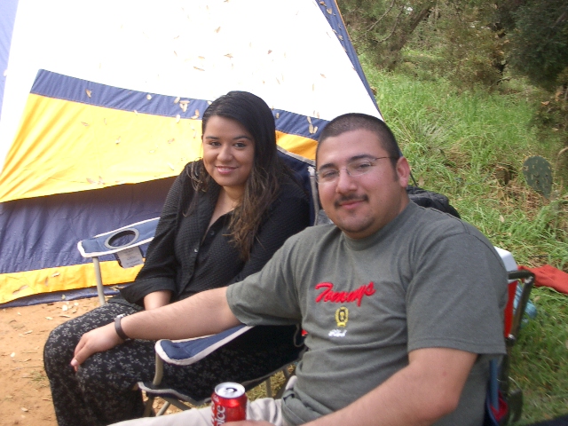 Man and woman sitting in camping chairs in front of a tent. A can of soda is on the ground