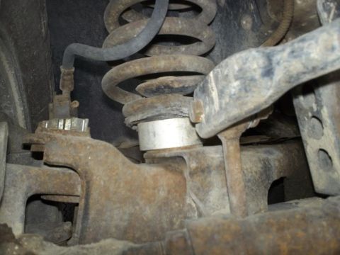 1987 Ford Bronco II - This image shows the rusty suspension system of a vehicle, focusing on the coil spring and brake line.