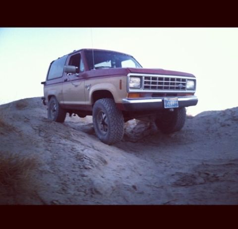 1987 Ford Bronco II - A two-tone 1987 Ford Bronco II navigates a dirt incline under a clear sky.