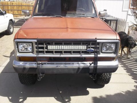 1987 Ford Bronco II - Front view of a 1987 Ford Bronco II with a light bar installed on the grille. A white SUV is visible to the left.