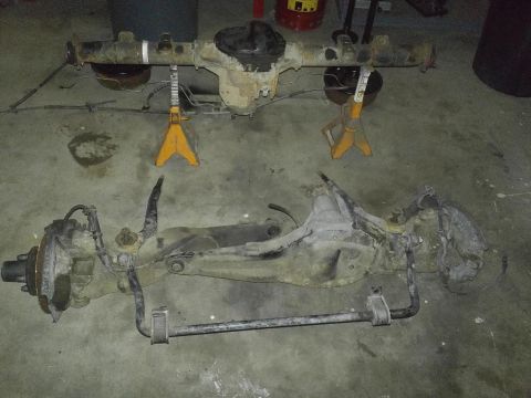 1987 Ford Bronco II - Disassembled vehicle axles and suspension components are laid out on a concrete floor, with one axle assembly elevated on jack stands.