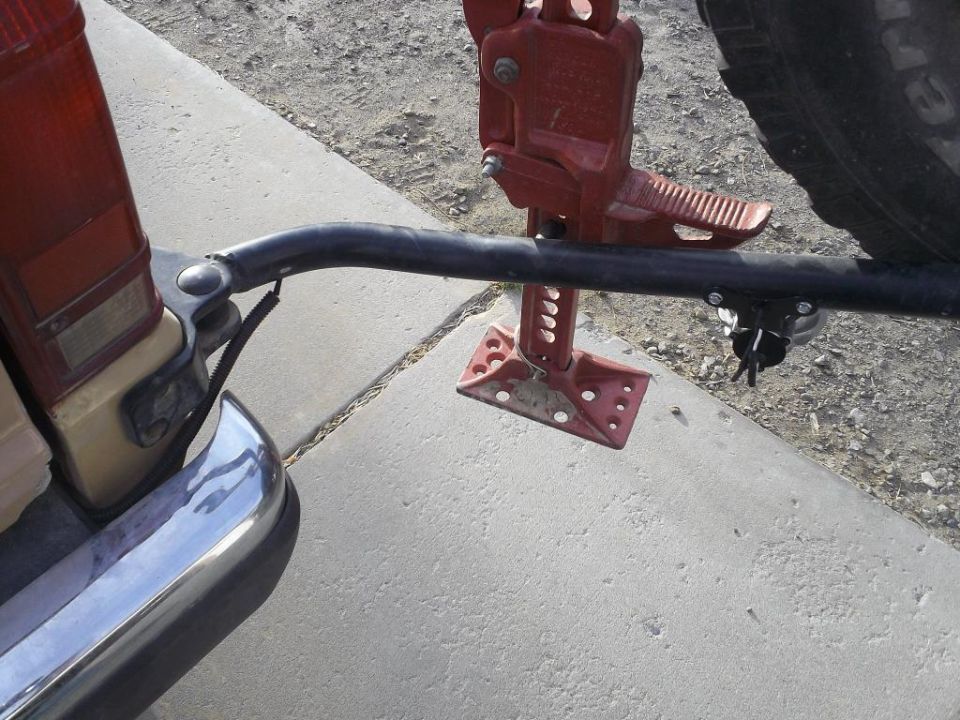 Vehicle rear bumper, taillight, and a hi-lift jack mounted on a rack. Spare tire visible