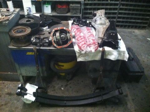1987 Ford Bronco II - Various automotive parts, including a differential and brake components, are laid out on a workbench.