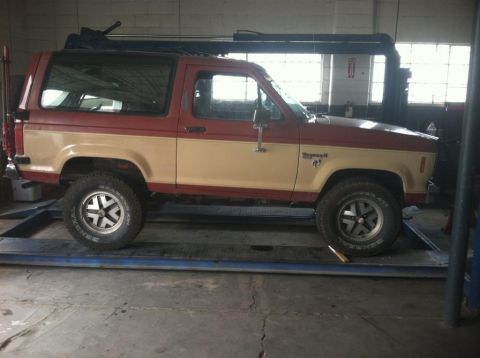 1987 Ford Bronco II - Side view of a 1987 Ford Bronco II in a garage, positioned on a lift.