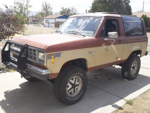 1987 Ford Bronco II - This two-tone Ford Bronco II is parked on a driveway with a white picket fence and houses in the background.