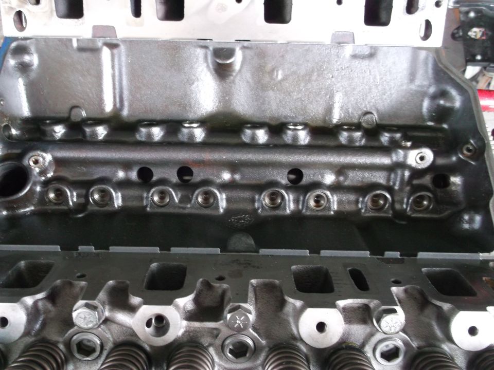Close-up of an engine block with cylinder head bolts and valve springs visible. Text reads 'SUPER MOTORS'