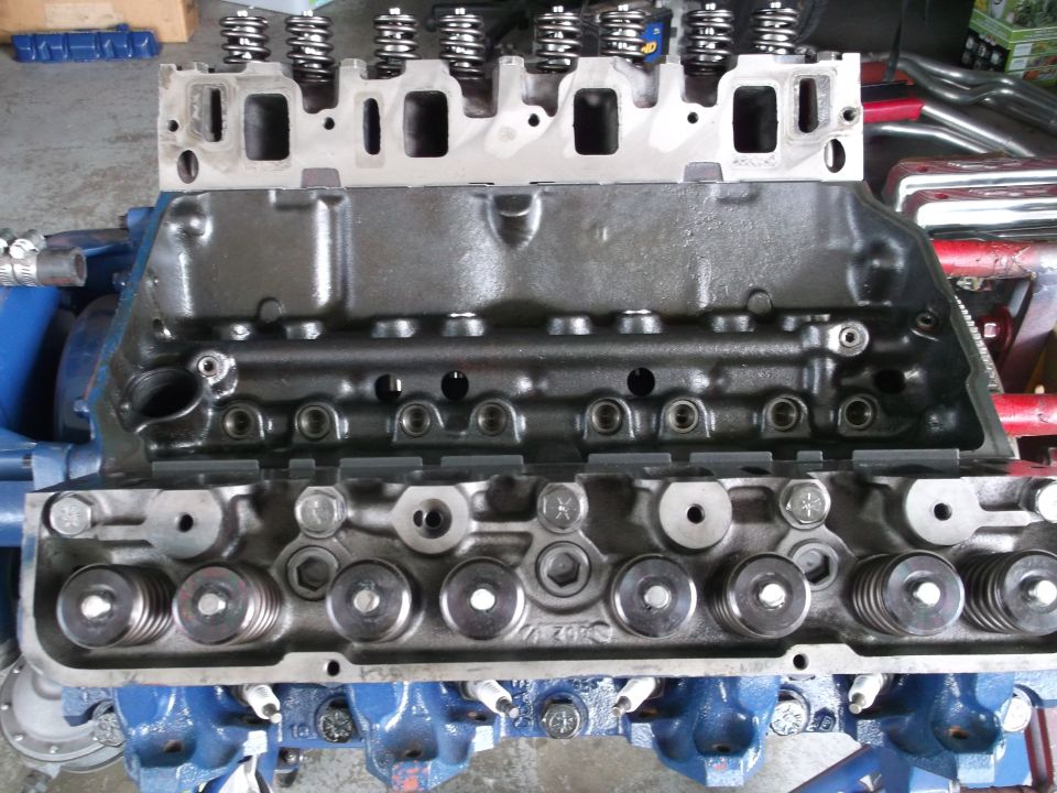 Overhead view of disassembled engine parts: cylinder heads with valve springs and a black-painted block section on a bench