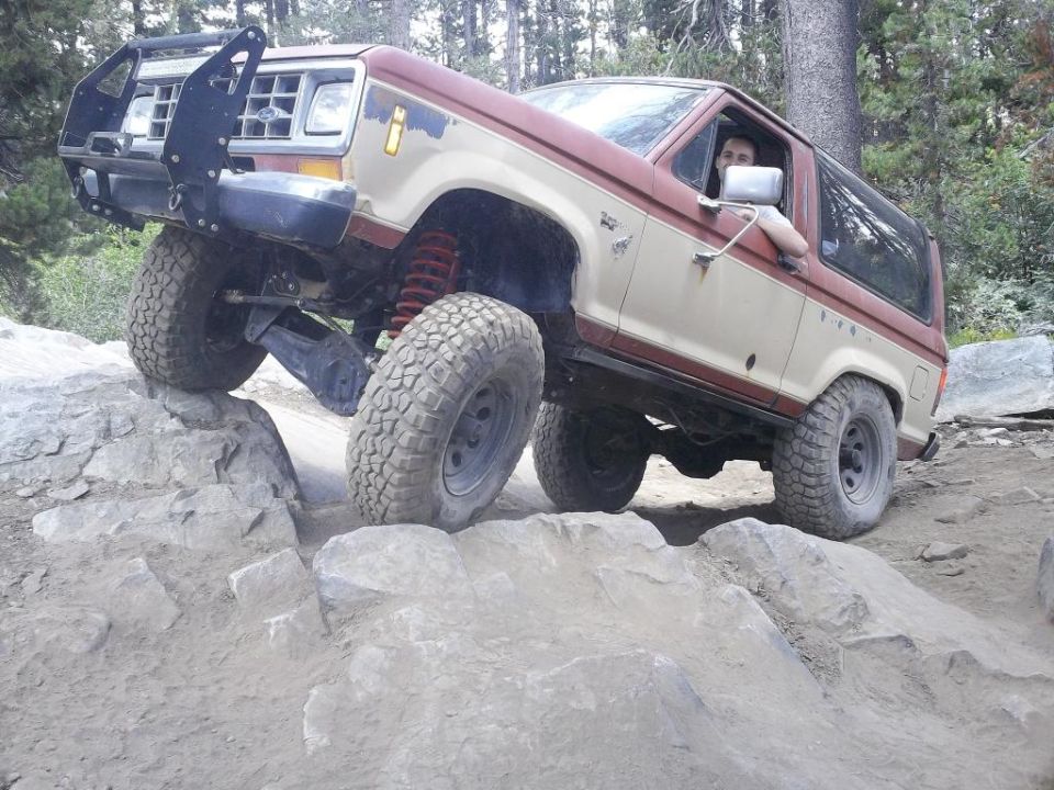 Tan and red 1987 Ford Bronco II off-roading over rocks, front-left tire elevated