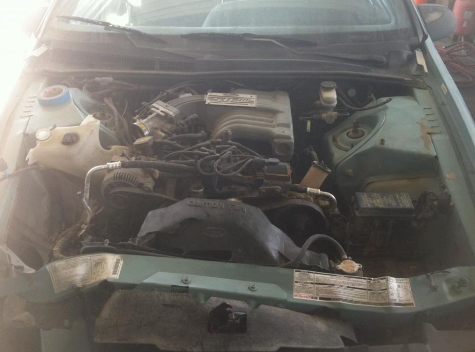 Engine bay with V6 engine, coolant reservoir, and various hoses. Green exterior paint visible