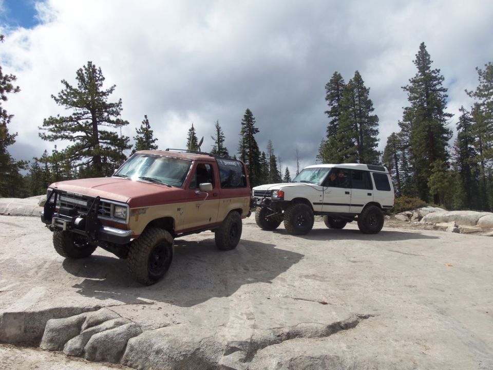 Red and tan Ford Bronco II with a brush guard and winch, and a white SUV parked on rocks