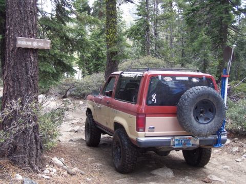 1987 Ford Bronco II - This 1987 Ford Bronco II is seen on a forest trail, equipped with a spare tire and shovel for off-road adventures.