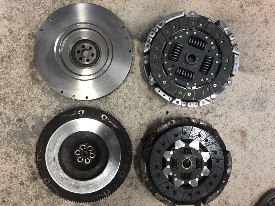 Two flywheels and two clutch pressure plates laid out on a concrete surface
