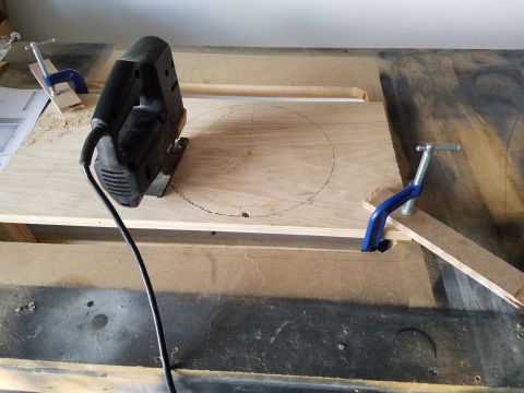 1994 Ford Bronco - Photograph of a jigsaw cutting a circular speaker opening in a plywood panel clamped to a workbench.