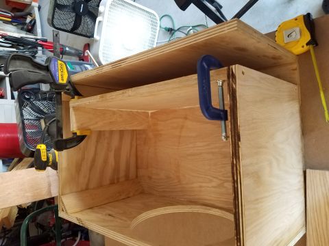 1994 Ford Bronco - Photograph of a plywood speaker enclosure held by clamps while glue sets in a workshop.