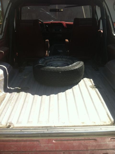 1984 Ford Bronco - The interior of a 1984 Ford Bronco is shown from the rear, with the tailgate open. A spare tire is placed in the cargo area, and the front…