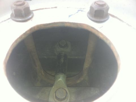 1984 Ford Bronco - This is a close-up, low-angle shot looking into a metal housing with a bolt and linkage assembly visible inside. Two nuts are visible on th…