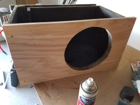 1994 Ford Bronco - Photograph of a plywood speaker enclosure with a dark-coated circular opening and a spray can on the bench.
