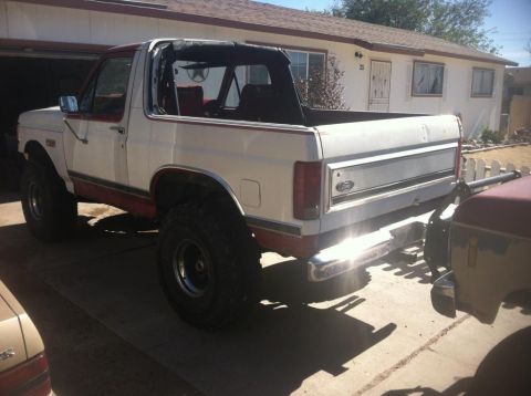 1984 Ford Bronco - The rear driver's side of a lifted, white and red 1980s Ford Bronco with a soft top is parked in a driveway in front of a house. The vehicl…