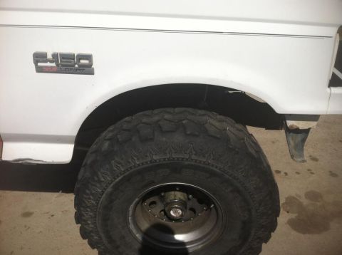 1984 Ford Bronco - A close-up view of the front fender and tire of a white Ford F-250 Lariat truck. The tire is a large, aggressive off-road tire with promine…