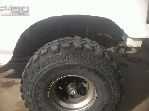 1984 Ford Bronco - A close-up view of the front fender well and tire of a white Ford F-250 XLT Lariat pickup truck. The fender liner has been removed, exposin…