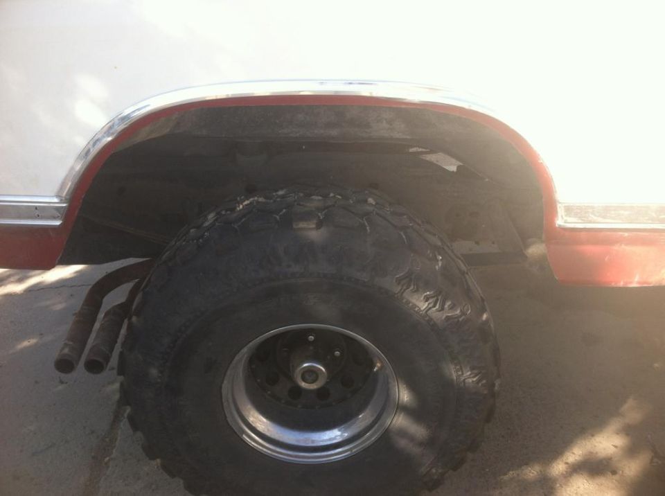 Side view of a large off-road tire and exhaust pipes under the wheel well of a white and red vehicle.