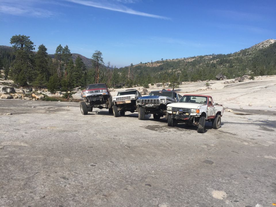 Four off-road trucks parked on a rocky surface.