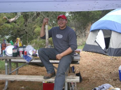 1994 Ford Bronco - Man with machete at a campsite with a tent and picnic table full of supplies.
