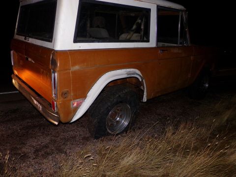 1969 Ford Bronco - Rear view of an orange and white Ford Bronco parked outdoors in the dark.