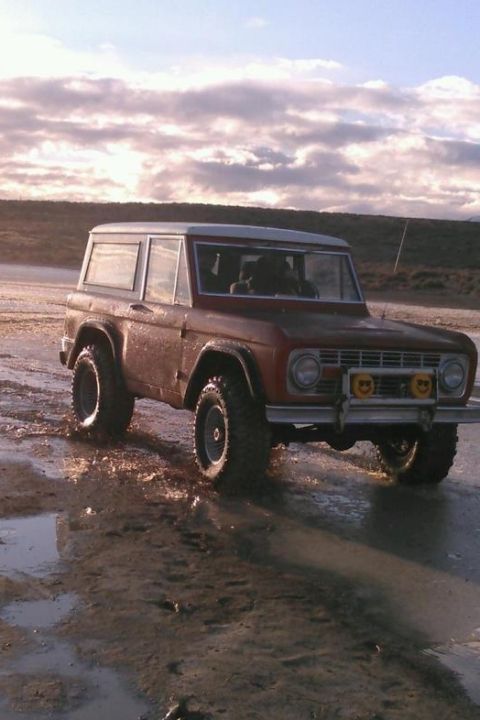 1969 Ford Bronco - A classic red Ford Bronco navigates a wet, muddy terrain under a cloudy sky.