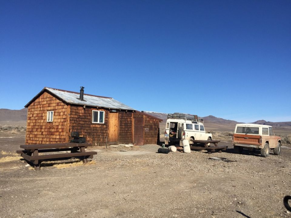 1969 Ford Bronco parked next to a white SUV and a wooden cabin.