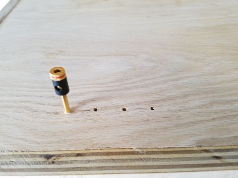 1994 Ford Bronco - Photograph of a gold speaker binding-post terminal installed in a plywood panel beside drilled pilot holes.