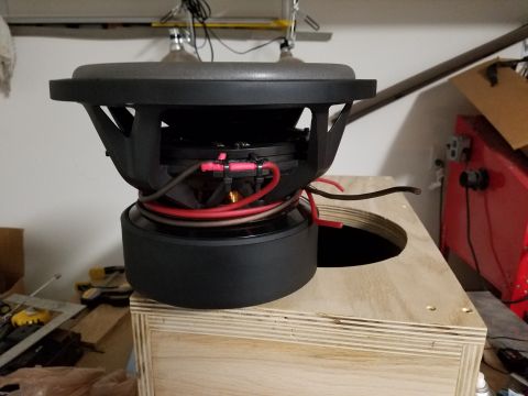 1994 Ford Bronco - Photograph of a subwoofer driver with red and black speaker wires being connected above an enclosure opening.