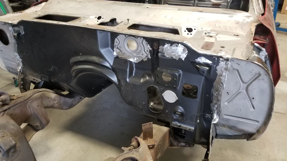 Classic car firewall and inner fender wells, some black, some bare metal with welds.