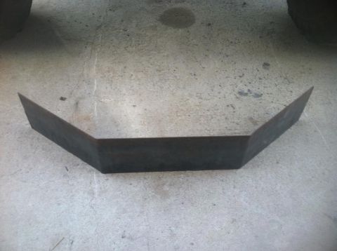1984 Ford Bronco - A dark metal, V-shaped bracket or reinforcement piece is shown resting on a concrete surface. The piece has two angled sections meeting at…