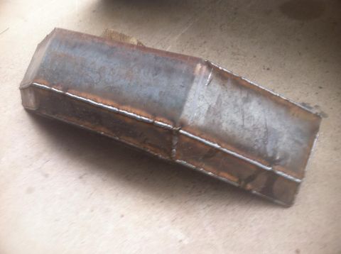 1984 Ford Bronco - A welded metal box with a tapered end sits on a light-colored surface. The metal appears rusted and shows visible weld lines.