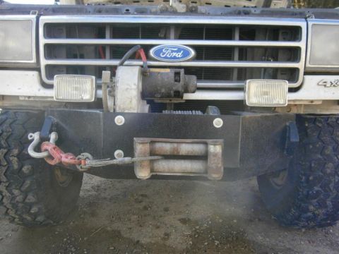 1984 Ford Bronco - The front of a Ford Bronco with a winch mounted on a custom bumper. A red tow hook is attached to the bumper and connected to the winch cab…