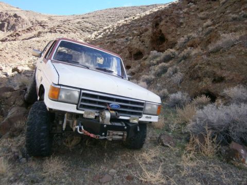1984 Ford Bronco - A white and red 1980s Ford Bronco is parked on a rocky, arid hillside. The vehicle is equipped with a winch mounted on the front bumper.