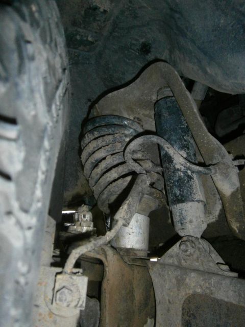 1984 Ford Bronco - A close-up, low-angle view of the suspension system of a 1984 Ford Bronco, showing the coil spring, shock absorber, and surrounding frame c…