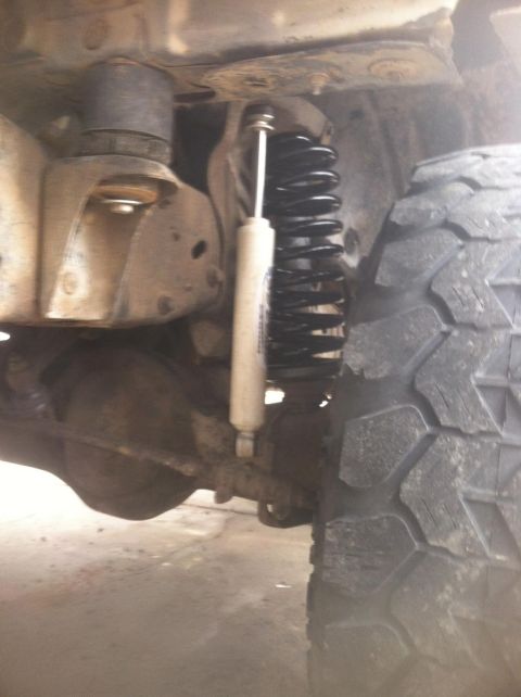 1984 Ford Bronco - A close-up view of the front suspension components of a 1984 Ford Bronco, featuring a black coil spring and a white shock absorber.