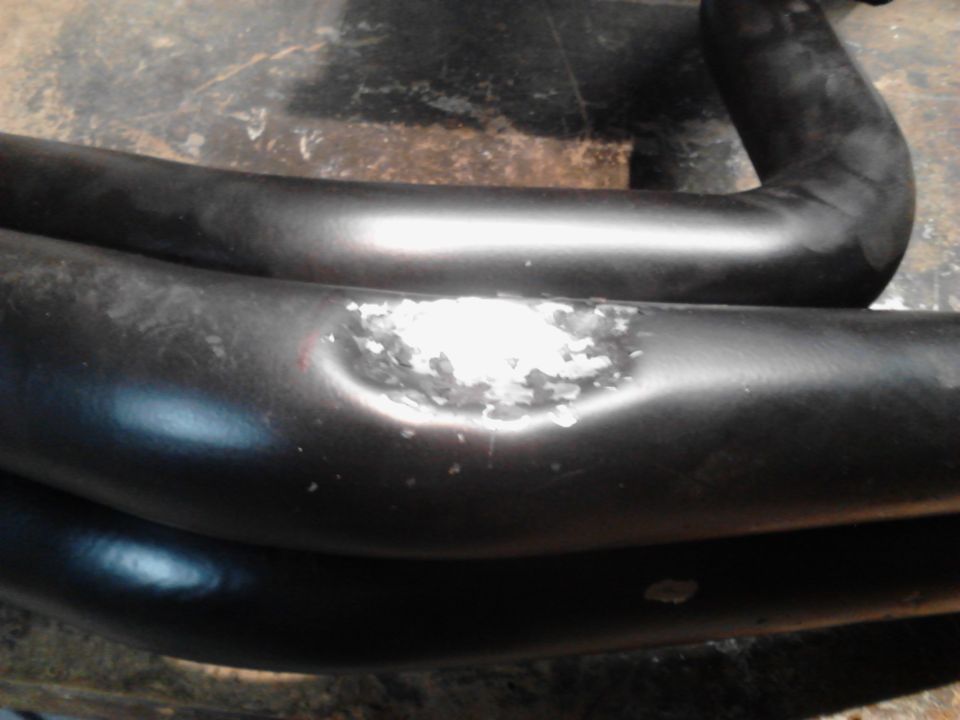 Close-up of two black exhaust pipes with chipped paint on the lower one.
