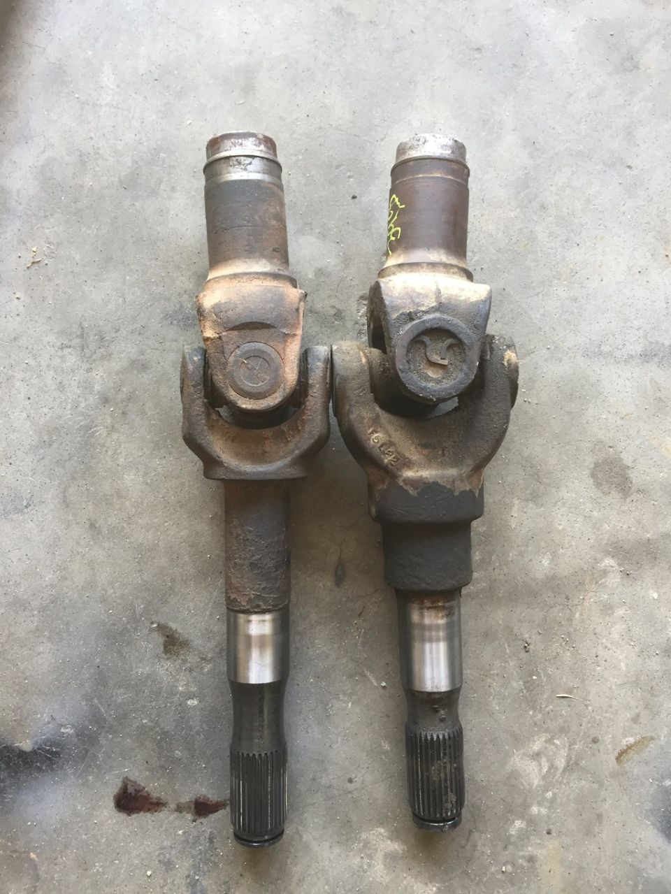 Two driveshaft U-joints side-by-side on a concrete surface