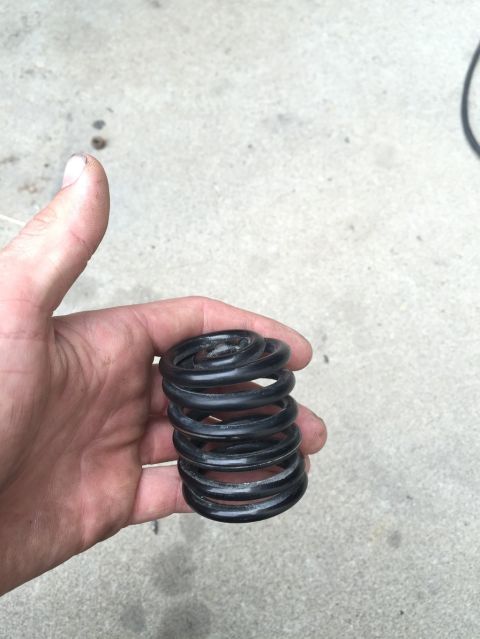 1984 Ford Bronco - A hand holds a black coil spring against a concrete background. The Supermotors.net logo is visible in the lower right corner.