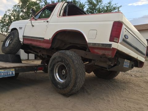 1984 Ford Bronco - White and red Ford Bronco loaded onto a trailer, showing its lifted suspension and large off-road tires.