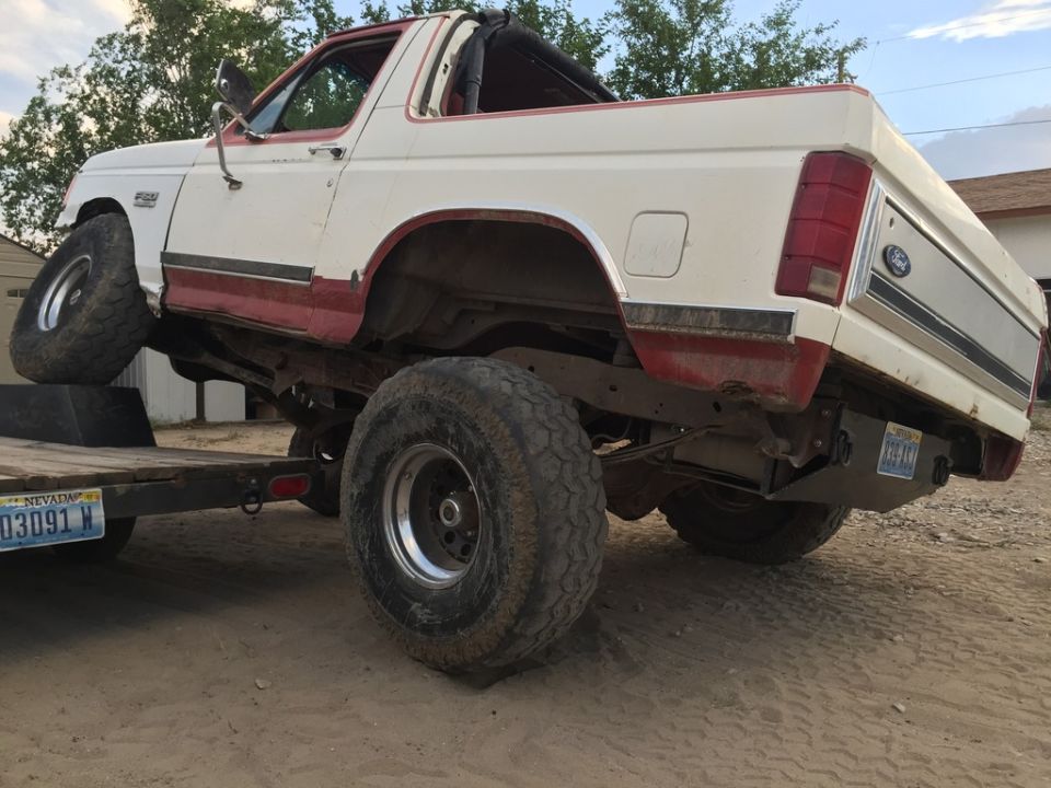 White and red Ford Bronco on a trailer, lifted with large tires